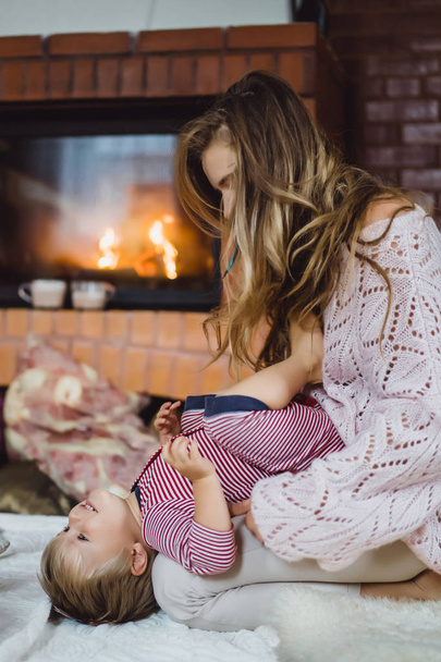 young woman with a child. Mom and son are fooling around, having fun near the fireplace. - Foto, afbeelding