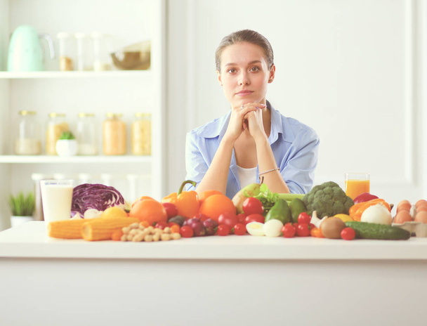 Young and cute woman sitting at the table full of fruits and vegetables in the wooden interior. - Foto, Imagen