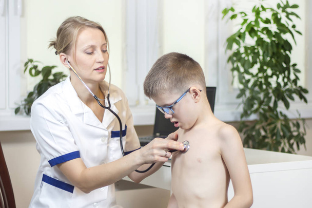 Kind während der ärztlichen Untersuchung in der Praxis eines Kinderarztes. ärztliche Untersuchung mit einem Bruststethoskop in einer Arztpraxis. der Junge mit dem offenen Mund atmet tief durch. - Foto, Bild