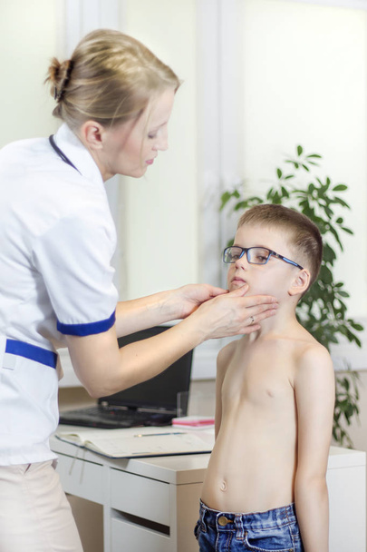 Doctor in a doctor's office while medical examining the tonsils of a boy with glasses. - Photo, Image