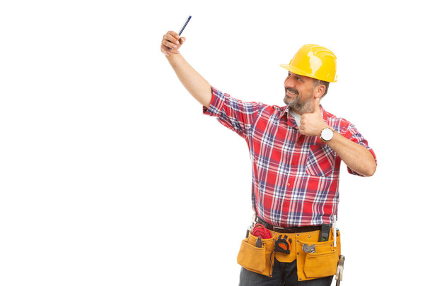 Happy friendly male builder taking selfie holding thumb up as like gesture isolated on white background - Photo, Image