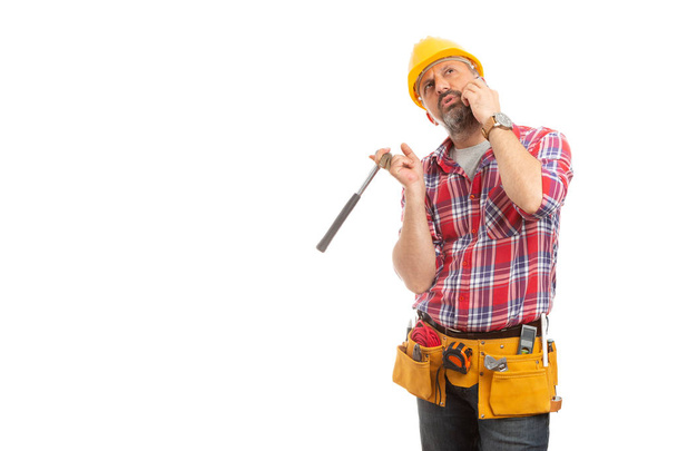 Capataz de construcción hablando por teléfono mientras sostiene el martillo y mira hacia arriba aislado sobre fondo blanco con espacio de copia en blanco
 - Foto, Imagen
