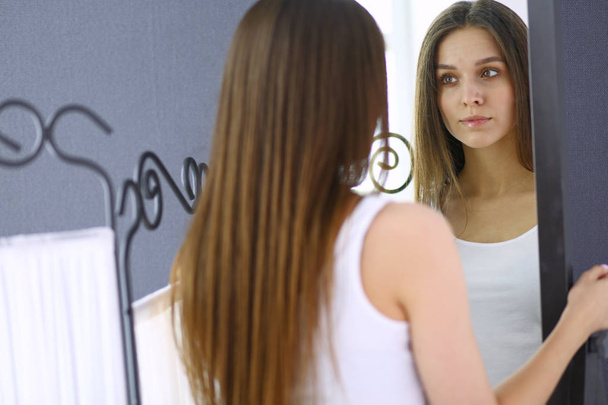 Молода жінка дивиться на себе відображення в дзеркалі вдома
. - Фото, зображення