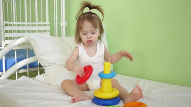 Children Kid and Baby play on bed with a pyramid and colored rings. Educational toys for preschool and kindergarten children. Toy for girls. - Footage, Video