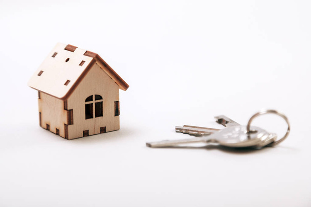 Houten miniatuur huis met deur sleutels close-up. Onroerend goed concept. Kleine toy houten huis met toetsen met kopie ruimte. - Foto, afbeelding