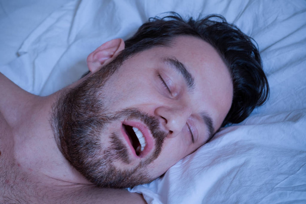Retrato de um homem dormindo na cama e roncando
 - Foto, Imagem