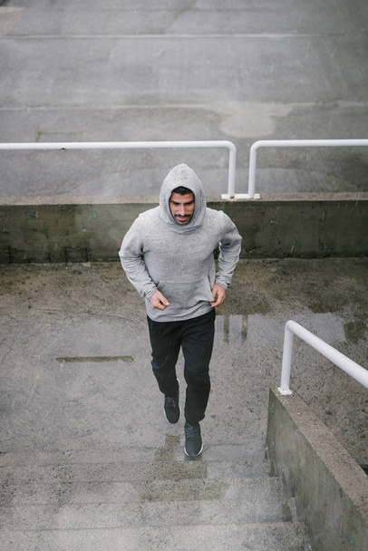 Urban athlete running upstairs under the rain. Banner of sporty man working out outside and climbing stairs in cold winter. - Valokuva, kuva