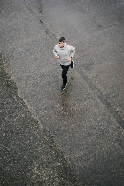 Top view of sporty man running in winter on urban asphalt. Male runner training outside. - Photo, image