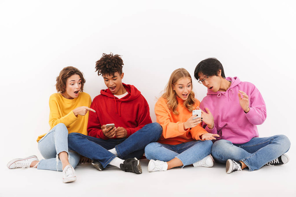 Group of cheerful multiracial friends sitting isolated over white, using mobile phones - Foto, immagini