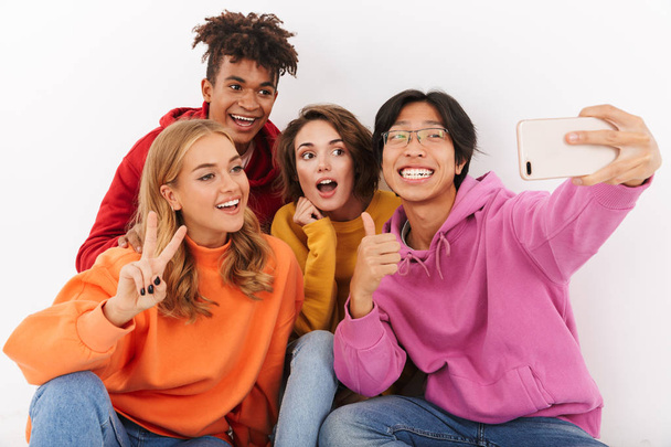 Group of cheerful teenagers isolated over white background, taking a selfie - Фото, изображение