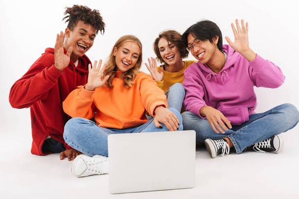 Image of young group of friends students isolated over white wall background using laptop computer waving. - Photo, Image