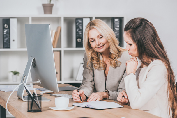 souriant mentor d'entreprise féminin pointant du doigt le cahier et travaillant avec un jeune collègue au bureau
 - Photo, image