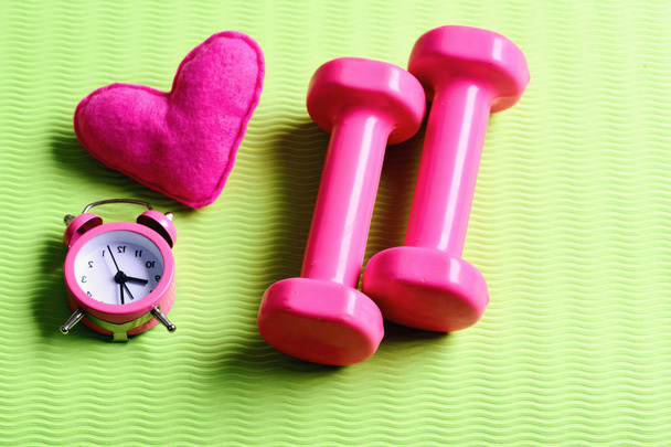 Dumbbells in pink color next to alarm clock and heart - Foto, imagen