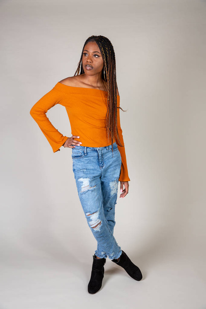 Studio shot of a young Black woman with vintage orange top and baggy jeans posing on a white background - Foto, imagen