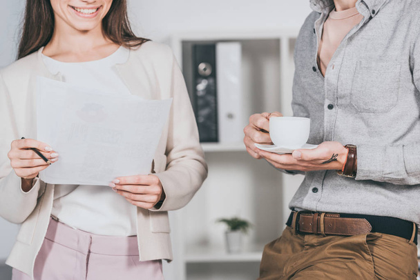 cropped shot of smiling business colleagues holding cup of coffee and papers in office - Fotografie, Obrázek
