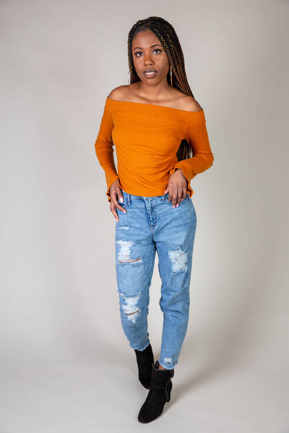 Studio shot of a young Black woman with vintage orange top and baggy jeans posing on a white background - Foto, Imagem