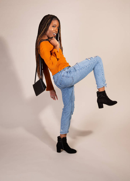 ビンテージ オレンジ トップ ダブダブのジーンズの財布と白の背景にポーズをとって若い黒人女性の撮影スタジオ - 写真・画像