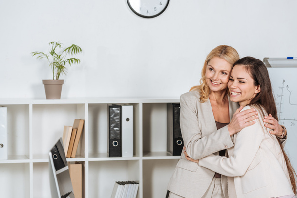 beautiful happy businesswomen standing together and looking away in office - Foto, Bild