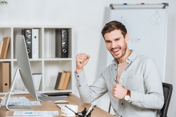happy young businessman triumphing and smiling at camera in office - Valokuva, kuva
