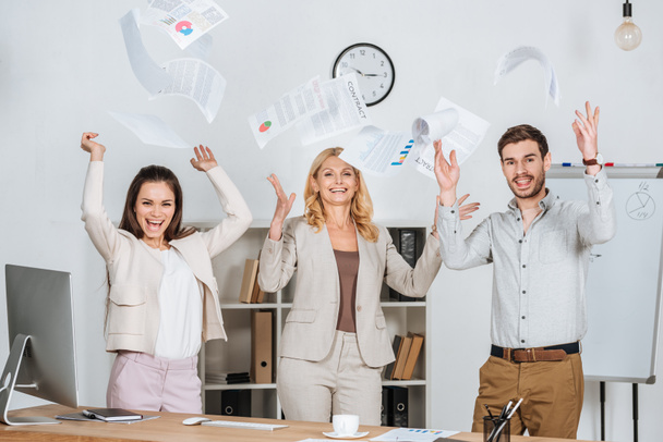 professzionális üzletemberek dobás papírok, és a kamera irodában mosolyogva izgatott   - Fotó, kép