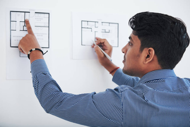 Adult ethnic office employee standing at white wall and checking blueprints - Photo, Image
