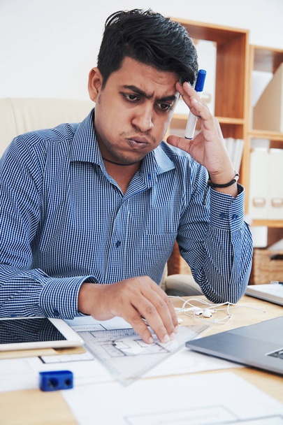 Уставший работник индийского офиса сидит за столом и выдыхает, прикасаясь к голове
 - Фото, изображение