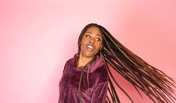 African American woman with amazing braided long hair in a casual urban lifestyle outfit on a pink backdrop - Foto, imagen