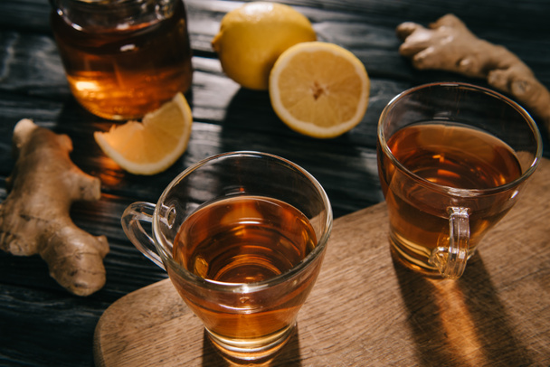 selective focus of  tea in glass cups on wooden chopping board with ginger roots and lemons - Foto, immagini