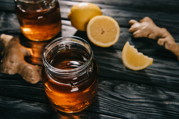 selective focus of  tea in glass jar on wooden table with ginger roots and lemons - Foto, afbeelding