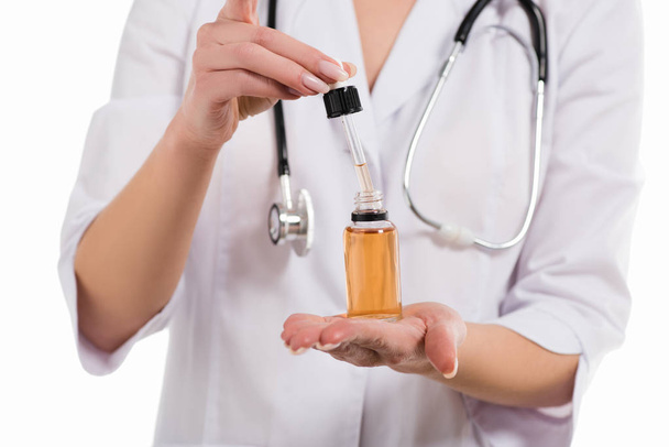 vista recortada de la botella de apertura del médico femenino con aceite y gotero aislado en blanco
 - Foto, imagen
