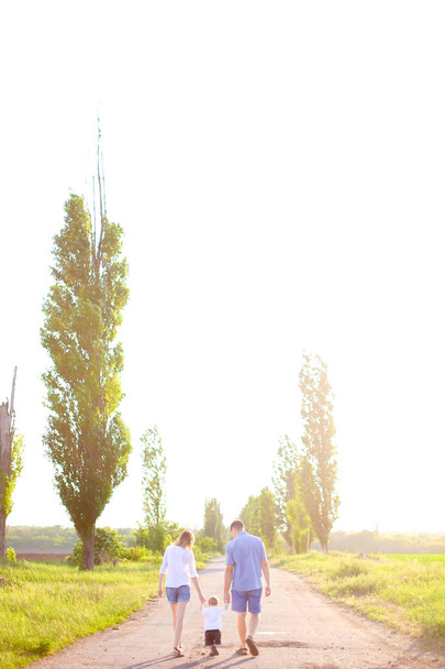 Joven madre y padre caminando por la carretera con un bebé pequeño, tiempo soleado
. - Foto, imagen