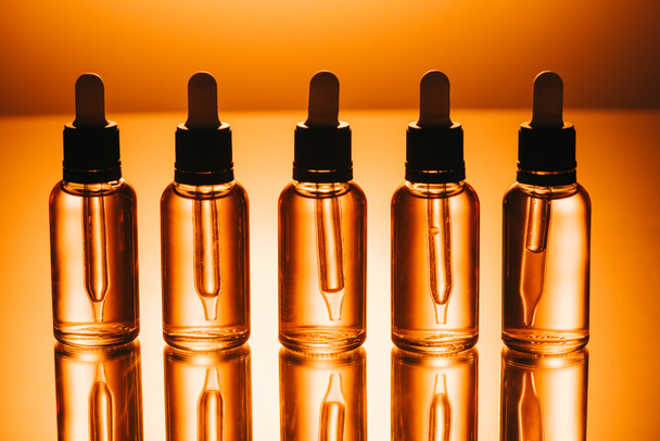 fila de aceite de cbd en botellas con goteros sobre fondo naranja
 - Foto, imagen