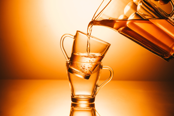 selective focus of two cups and teapot with stream tea on orange background - Foto, Imagem