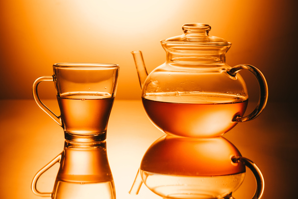 selective focus of cup of tea and teapot on orange background - Foto, imagen