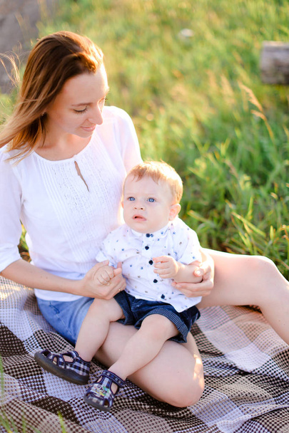 Young happy mother sitting with little child on plaid, grass on background. - Foto, imagen
