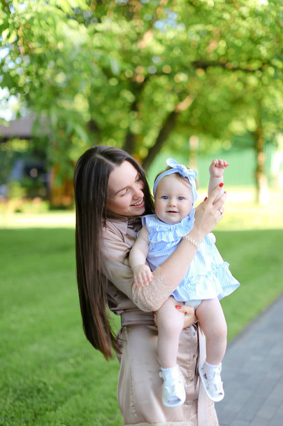 Mladá matka Kavkazský drží malá holčička v zahradě. Pojem mateřství a odpočinek v přírodě. - Fotografie, Obrázek