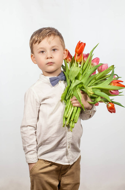 Cute little boy holding a bouquet of flowers. Tulips. Mothers Day. International Womens Day. Portrait of a happy little boy on - Фото, изображение