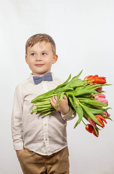 Милый мальчик с букетом цветов. Тюльпаны. День Матери. Международный женский день. Портрет счастливого мальчика на
 - Фото, изображение