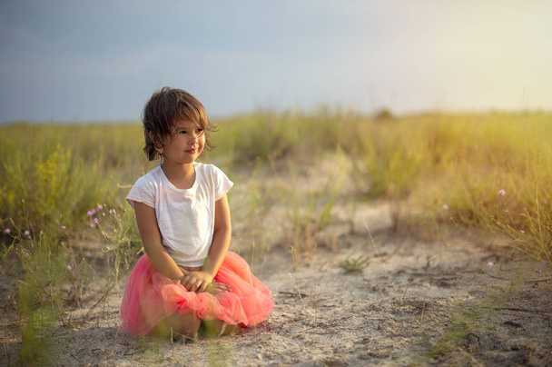cute little girl sitting on sandy hill on summer beach - Foto, imagen