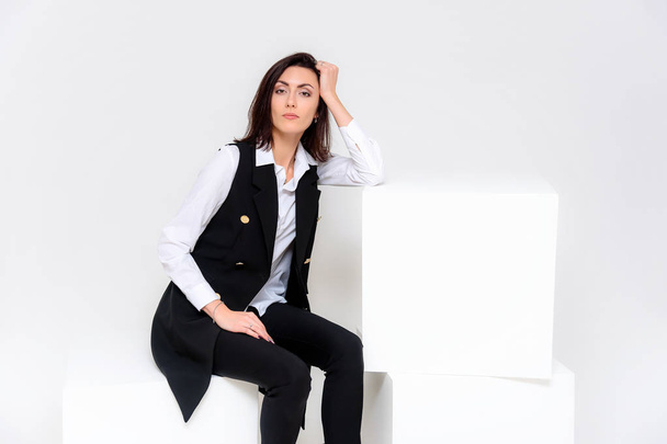 Concept portrait of a girl sitting on a white background in a business suit in different poses with different emotions. It in the middle of the frame, next to the white cubes, next is another cube. - Foto, Imagem