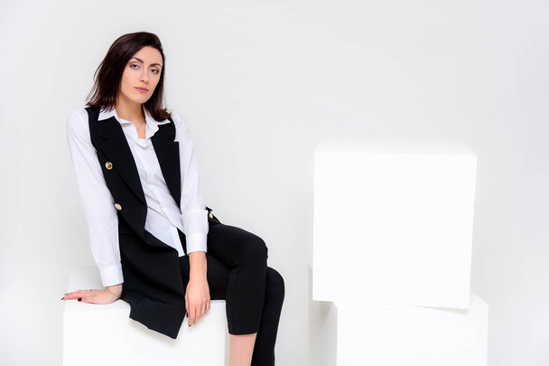 Concept portrait of a girl sitting on a white background in a business suit in different poses with different emotions. It in the middle of the frame, next to the white cubes, next is another cube. - Photo, Image