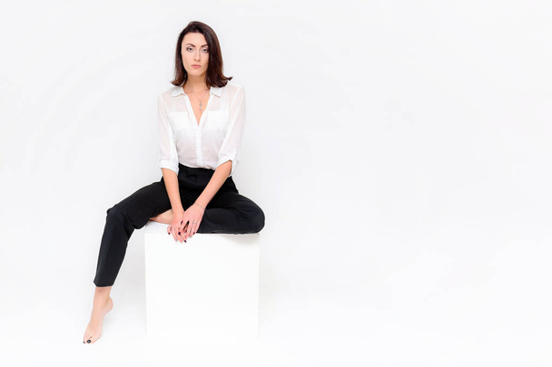 Concept portrait of a girl sitting on a white background in a business suit in different poses with different emotions. It in the middle of the frame, next to the white cubes, next is another cube. - Фото, изображение