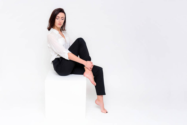 Concept portrait of a girl sitting on a white background in a business suit in different poses with different emotions. It in the middle of the frame, next to the white cubes, next is another cube. - Photo, image