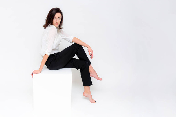 Concept portrait of a girl sitting on a white background in a business suit in different poses with different emotions. It in the middle of the frame, next to the white cubes, next is another cube. - Foto, afbeelding