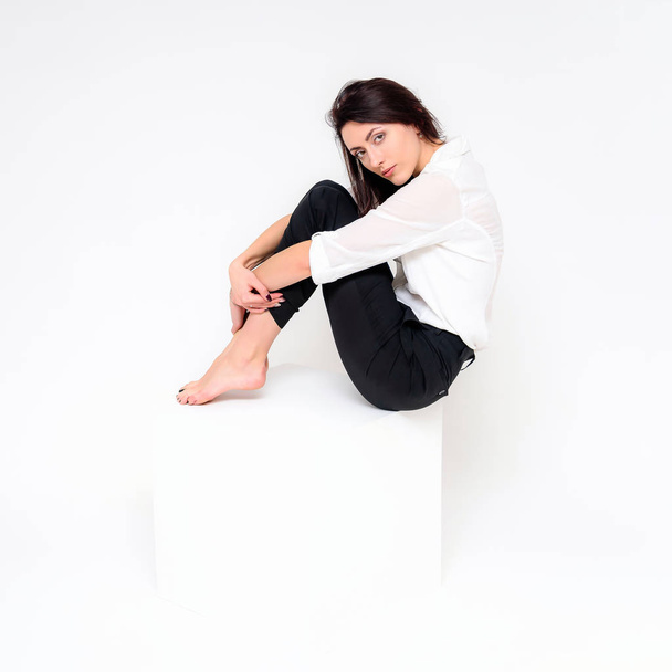 Concept portrait of a girl sitting on a white background in a business suit in different poses with different emotions. It in the middle of the frame, next to the white cubes, next is another cube. - Foto, immagini