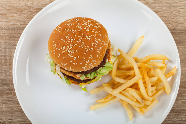 Fresh tasty double cheeseburger with beef, cheddar and lettuce and french fries on a white plate, wooden table - Foto, Imagem