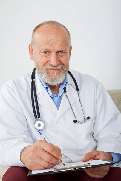 Udane starszy mężczyzna lekarz wypełniając formularz diagnozy, siedzi na kanapie w urzędzie - Zdjęcie, obraz