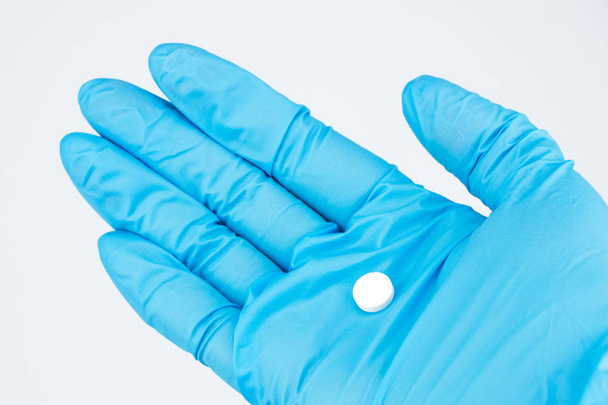 Szczegół dłoń w rękawicy niebieski. Na dłoni lekarz leży jeden Białe okrągłe tabletki. Tło jest białe - Zdjęcie, obraz
