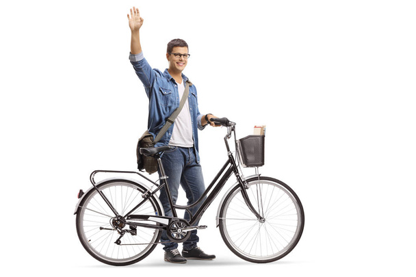 Full length shot of a casual young man with a bicycle waving isolated on white background - Valokuva, kuva