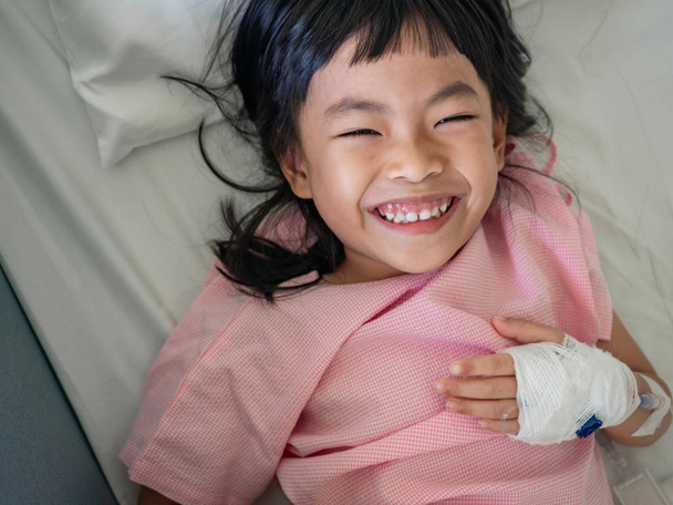 Azjatycki dziecko dziewczynka w szpitalu z pozytywnego nastroju. Duże uśmiechający się na łóżku. - Zdjęcie, obraz